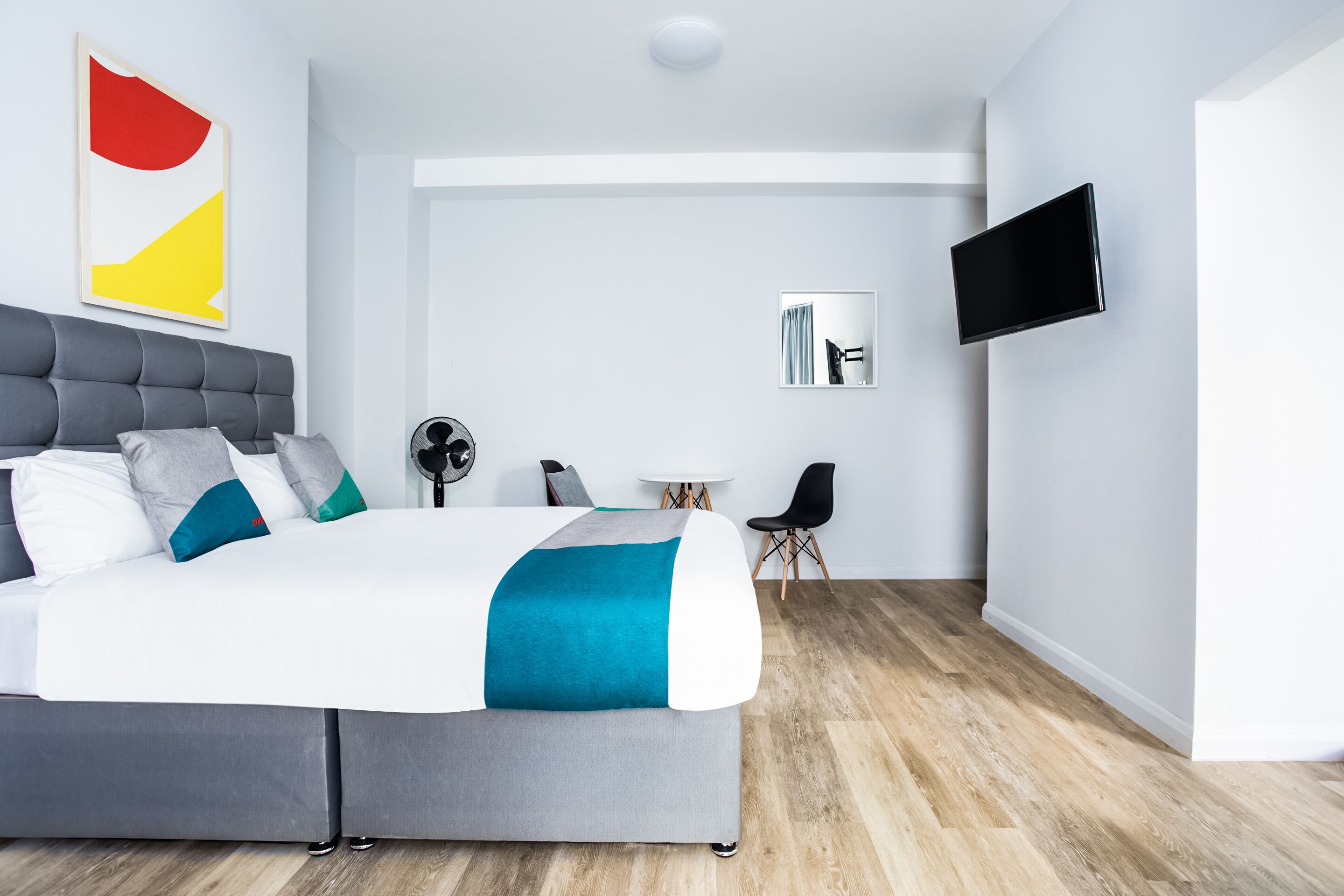 A modern hotel room with a large bed, a flat-screen TV, a small table, and a chair.