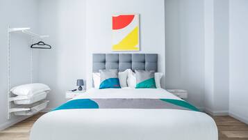 A modern bedroom with a large bed, a bedside table, a hanging light, and a wall-mounted artwork.