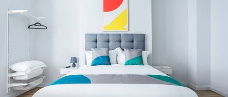 Un dormitorio moderno con una cama grande, una mesita de noche, una lámpara colgante y una obra de arte en la pared.