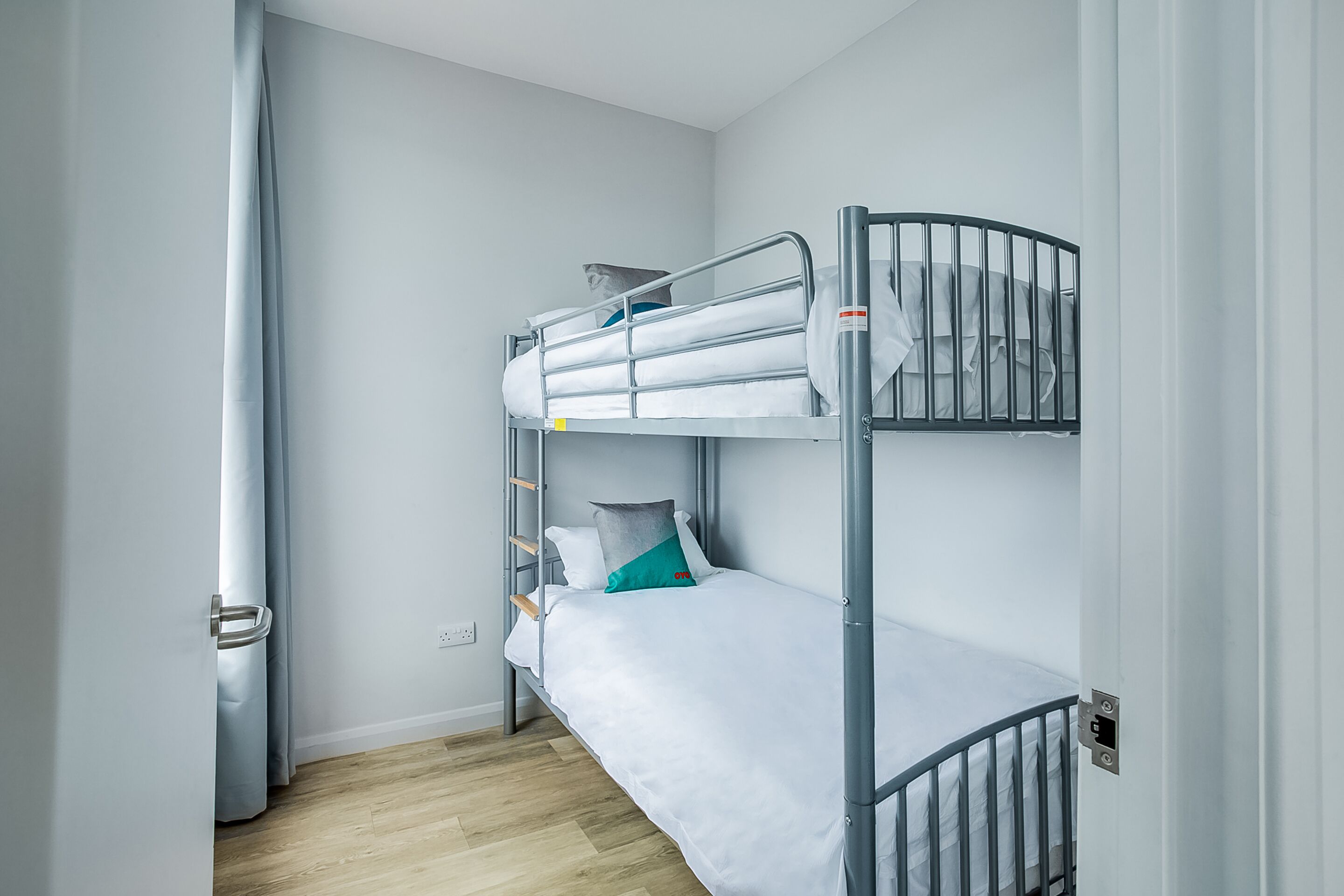 Een slaapkamer met een stapelbed, een metalen frame, wit beddengoed en een houten vloer.