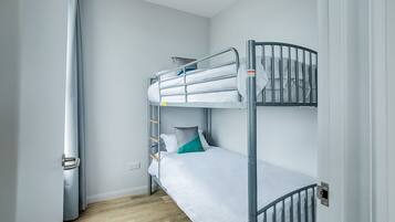 Een slaapkamer met een stapelbed, een metalen frame, wit beddengoed en een houten vloer.