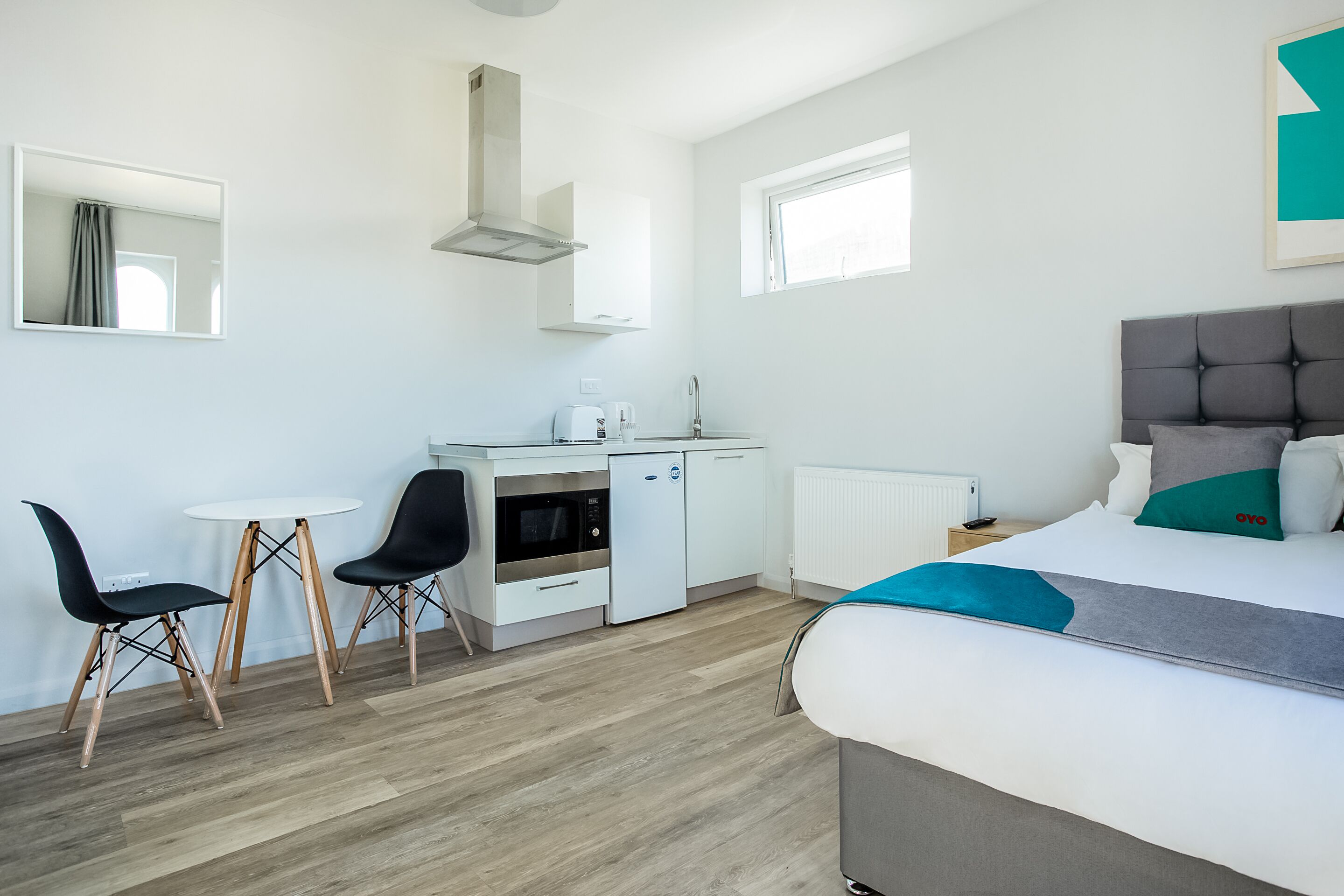 Een moderne hotelkamer met een bed, een bureau met stoel, een kitchenette en een raam.