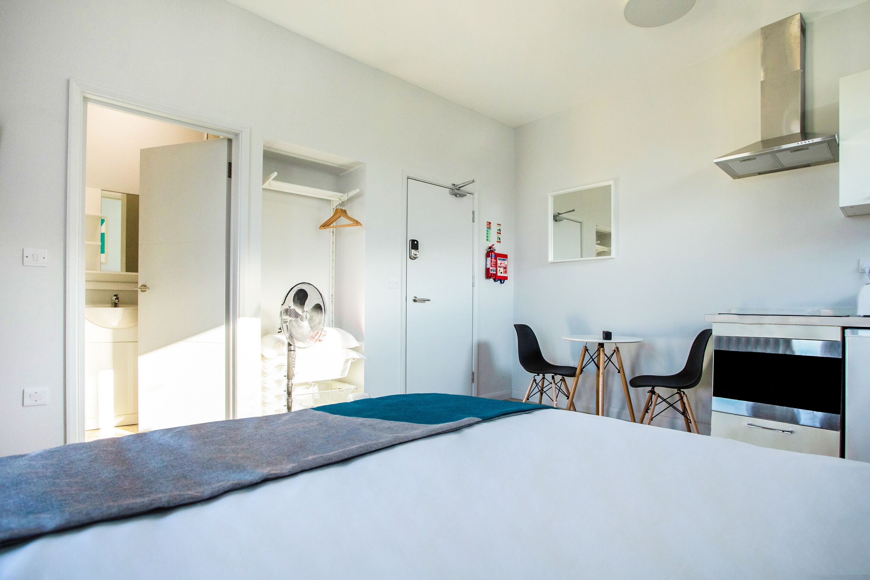 Een moderne hotelkamer met een bed, een bureau, twee stoelen, een bijzettafeltje, een spiegel en een kledingkast.
