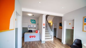 Zona de recepción con suelo de madera, un mostrador de recepción con la leyenda "OYO", una escalera y una silla negra.