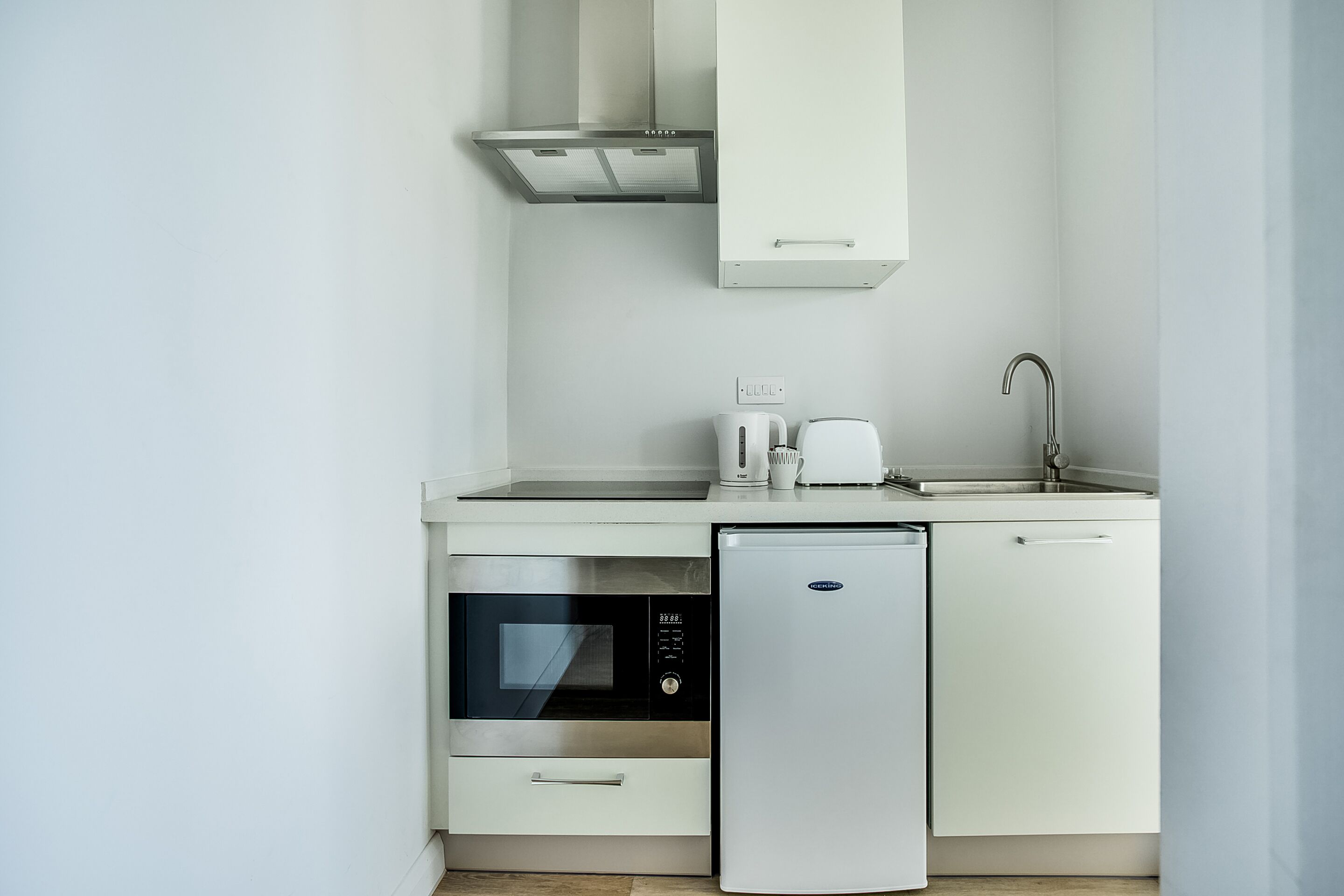 A compact kitchen with a built-in oven, a compact refrigerator, a coffee maker, and a sink.
