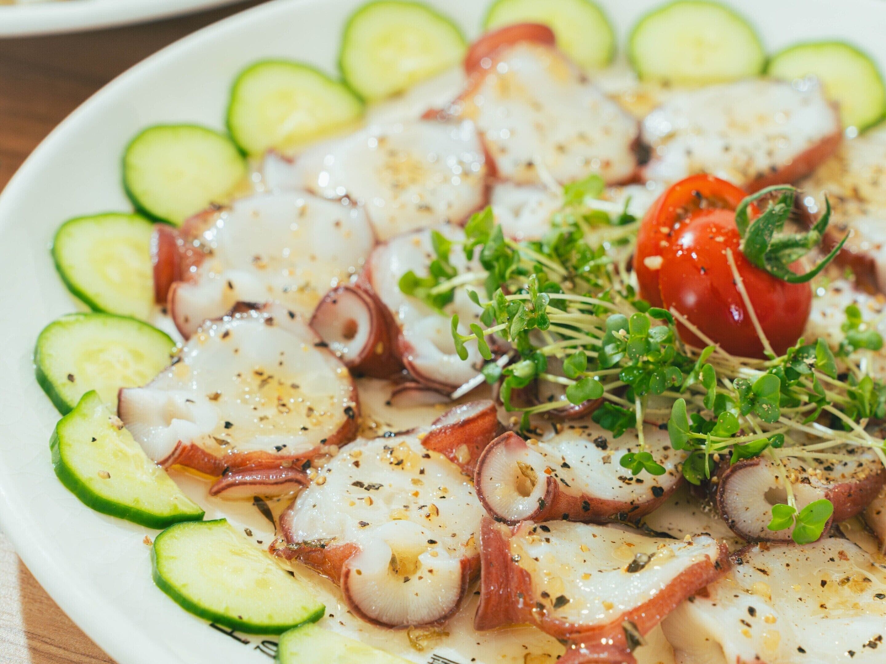 Ensalada de pulpo con rodajas de pepino y tomate cereza como adorno.