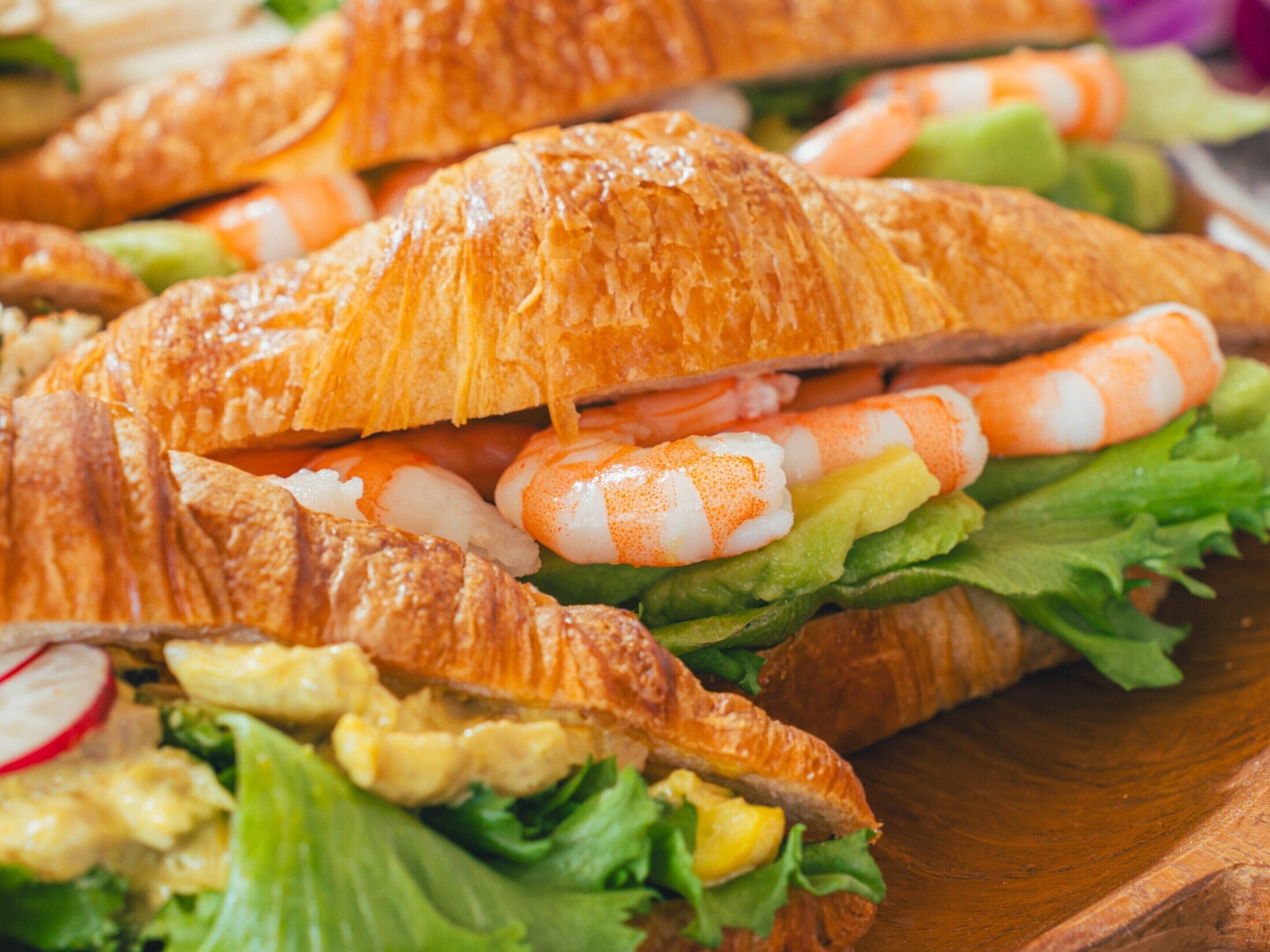 A sandwich with shrimp, lettuce, and a croissant.