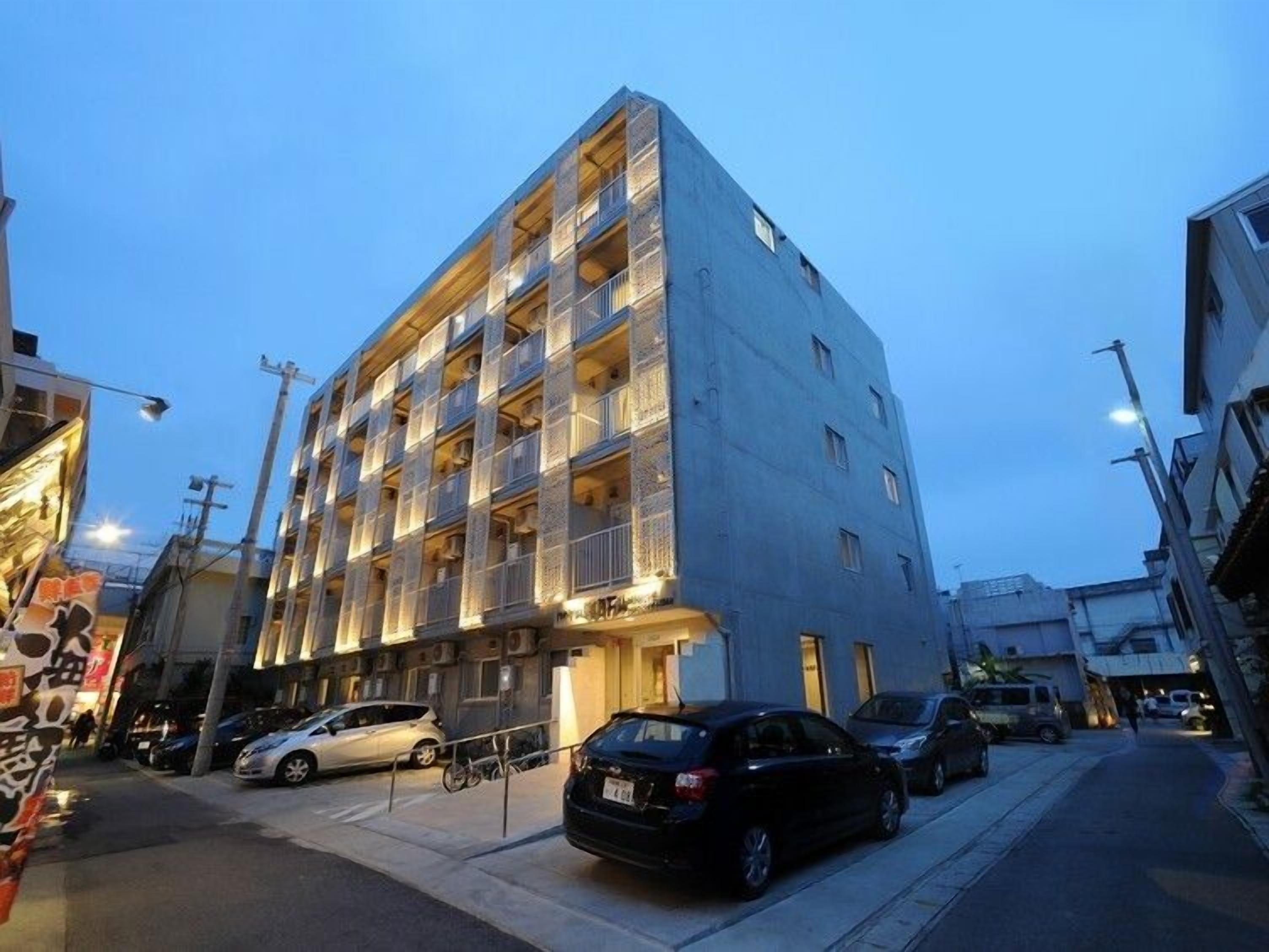 A multi-story building with balconies, parked cars, and a street lamp.