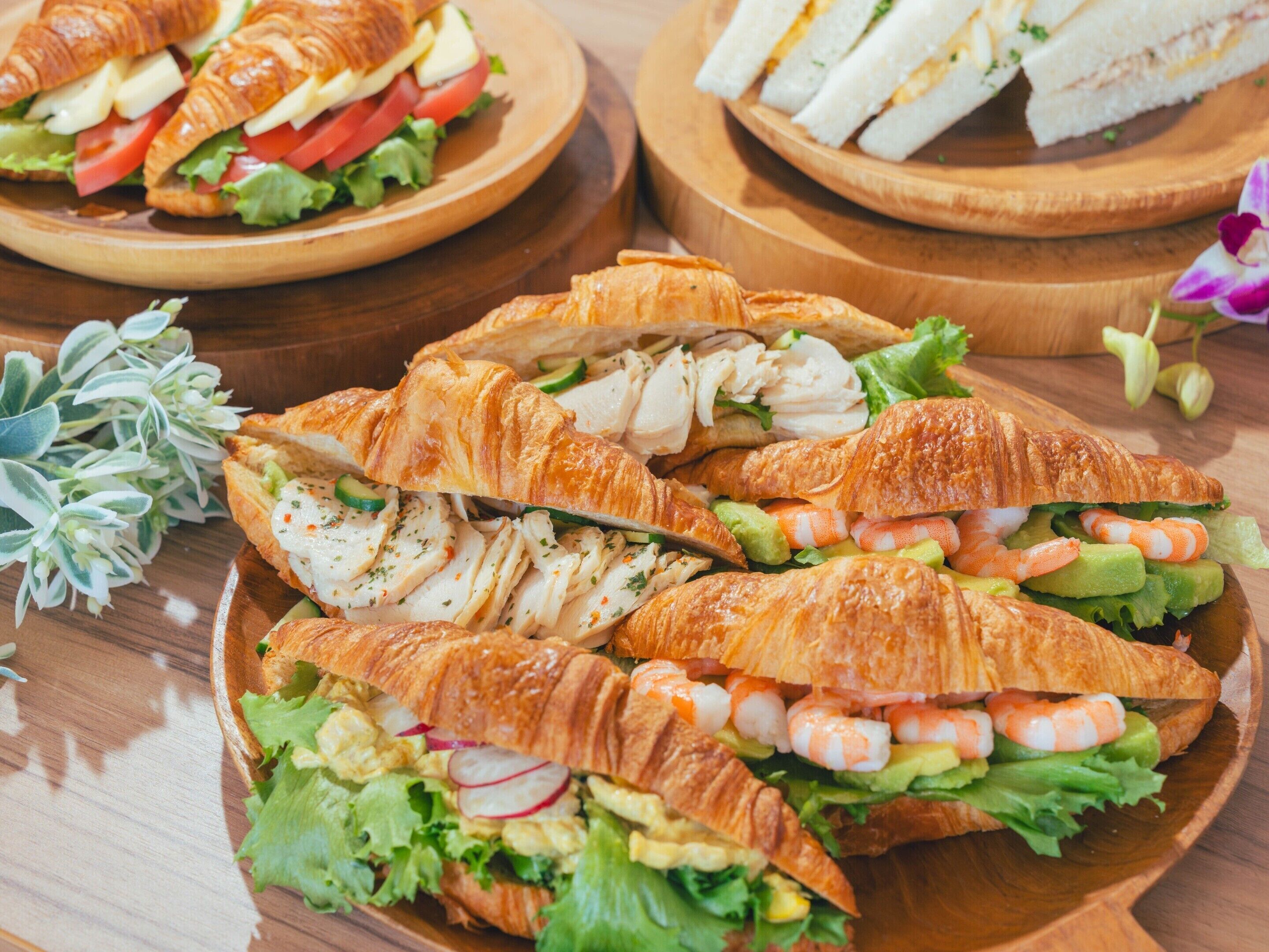 Une table en bois sur laquelle sont disposées trois assiettes de sandwichs, chacun garni d’une farce différente.