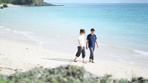 Two people walking on a beach with a clear view of the ocean and a small island in the distance. - The BREAKFAST HOTEL MARCHE Ishigakijima (Ishigaki)