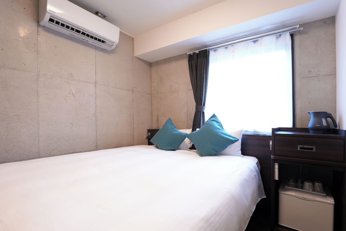 Quarto de hotel com cama, mesa de cabeceira, cafeteira e aparelho de ar condicionado.