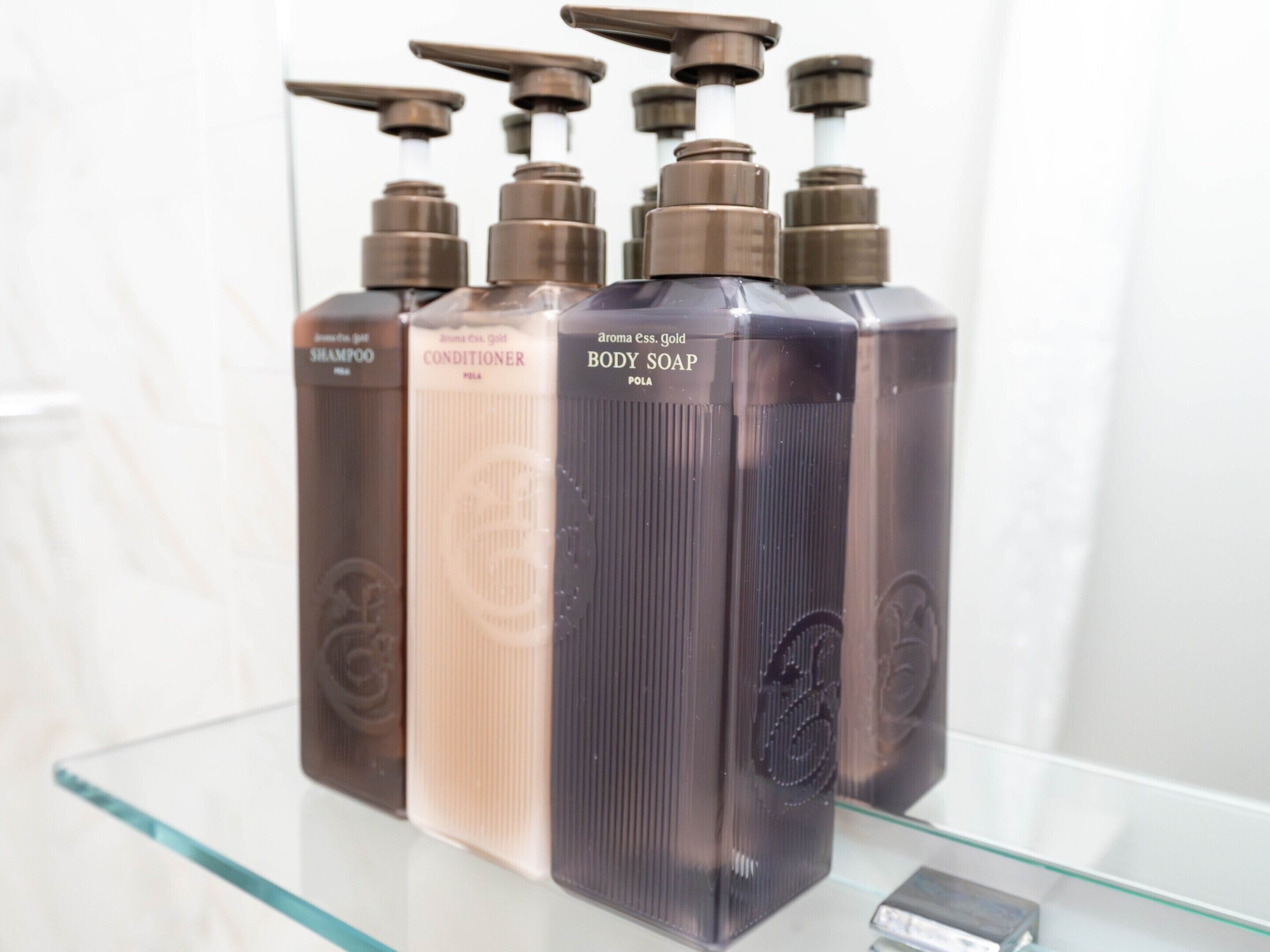 A row of three bottles of body soap on a glass shelf.