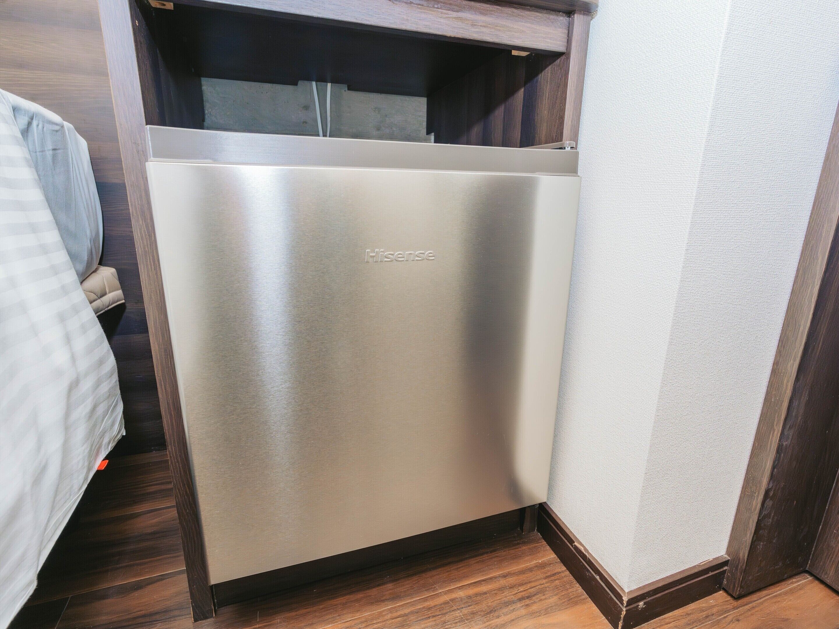 Un refrigerador metálico y compacto en un rincón de una habitación con suelo de madera y pared con textura.