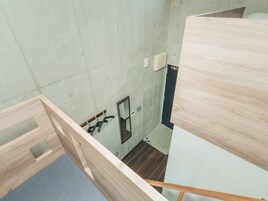 Una habitación con techo alto, piso de madera, un espejo pequeño y un interruptor de luz en la pared.