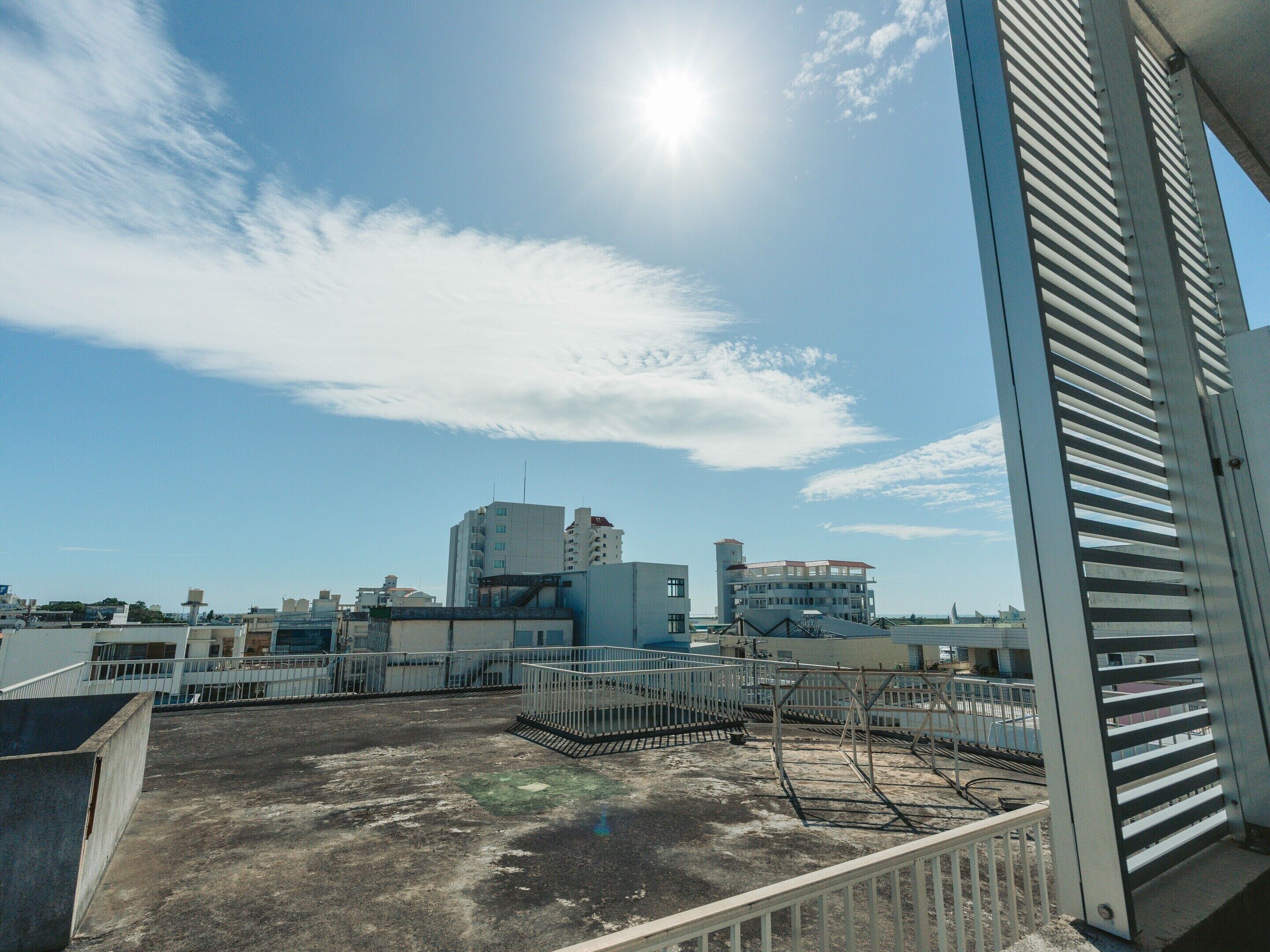 A rooftop view with buildings in the background, a clear sky, and a sun shining.