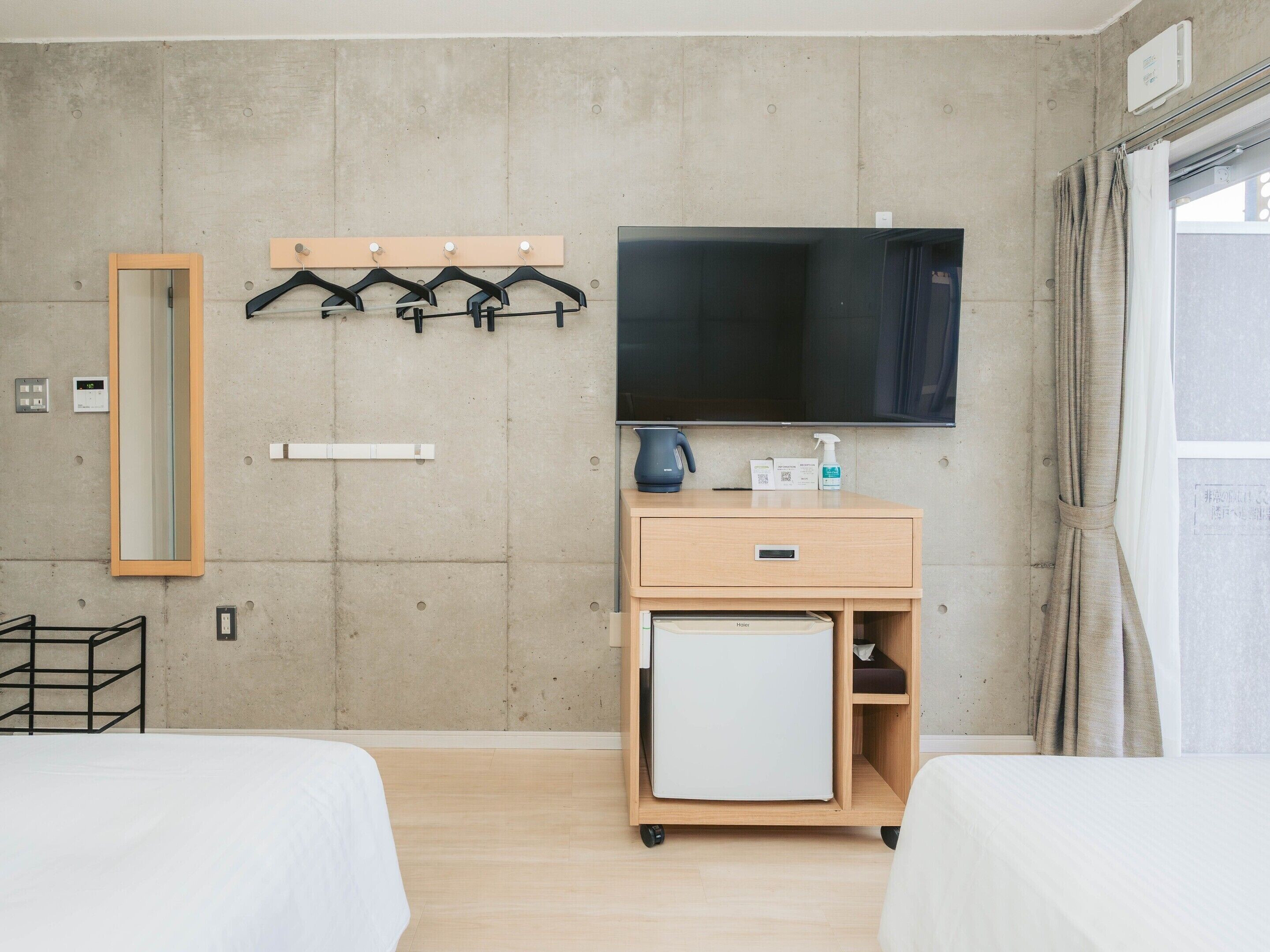 Ein Hotelzimmer mit zwei Betten, einem Fernseher, einer kleinen Kühlbox, einem Spiegel und einem Kleiderhaken.