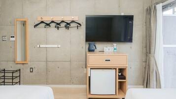 A hotel room with two beds, a TV, a small fridge, a mirror, and a coat rack.