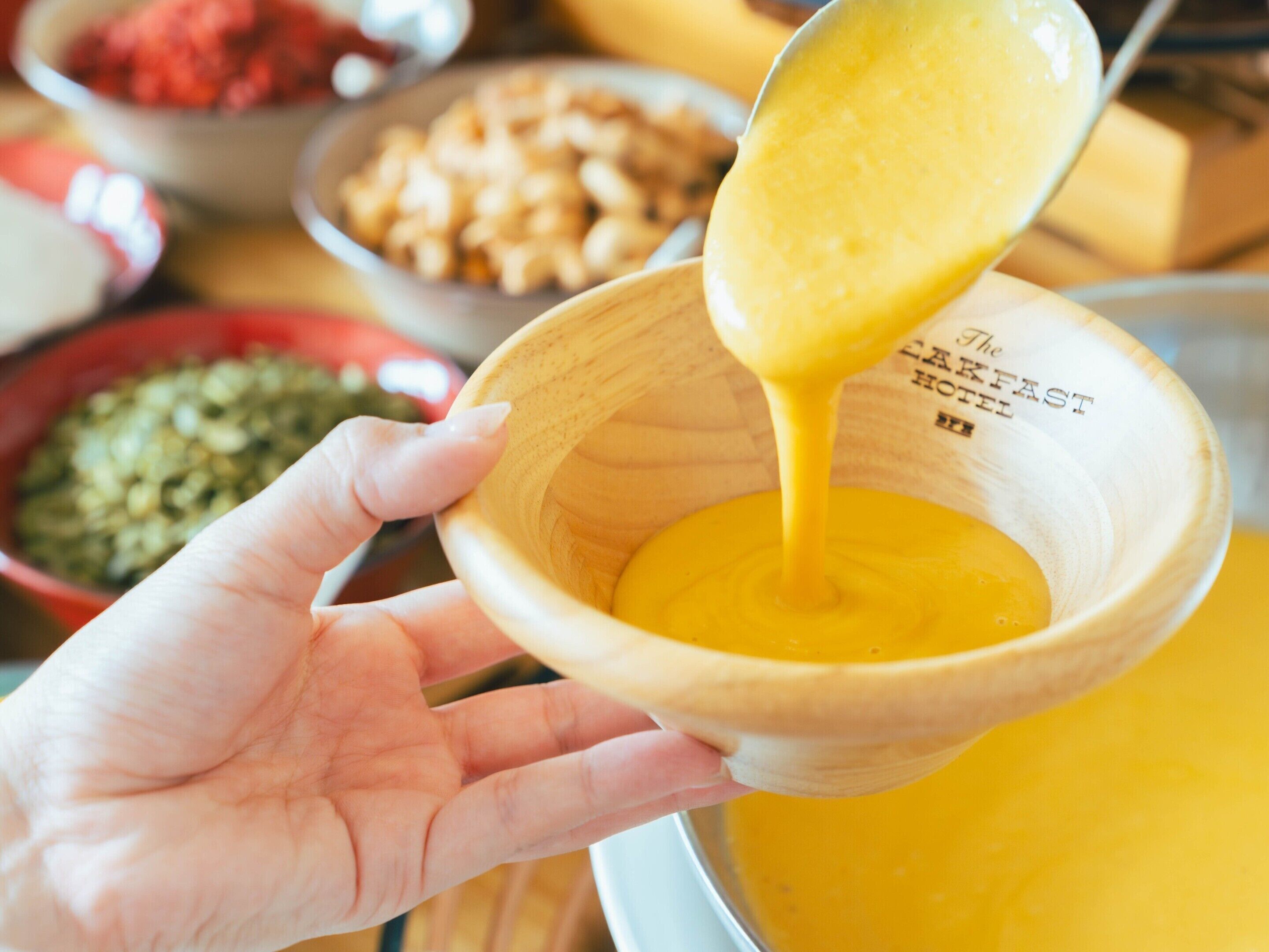 Un bol en bois dans lequel on verse une cuillère de liquide jaune.