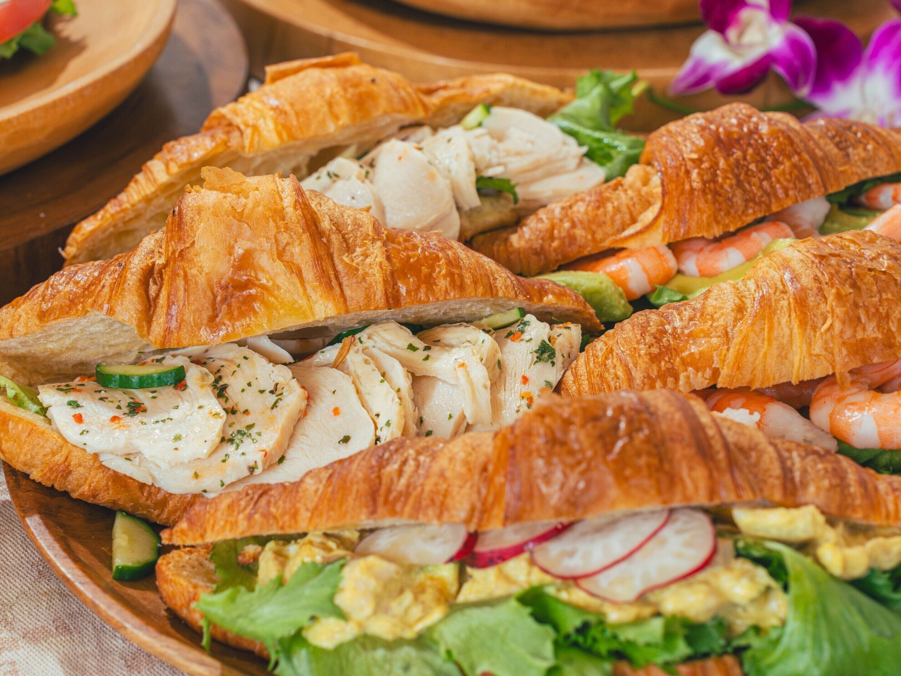 Egy tálca, tele ételekkel: van benne croissant, csirke, garnéla és zöldségek.
