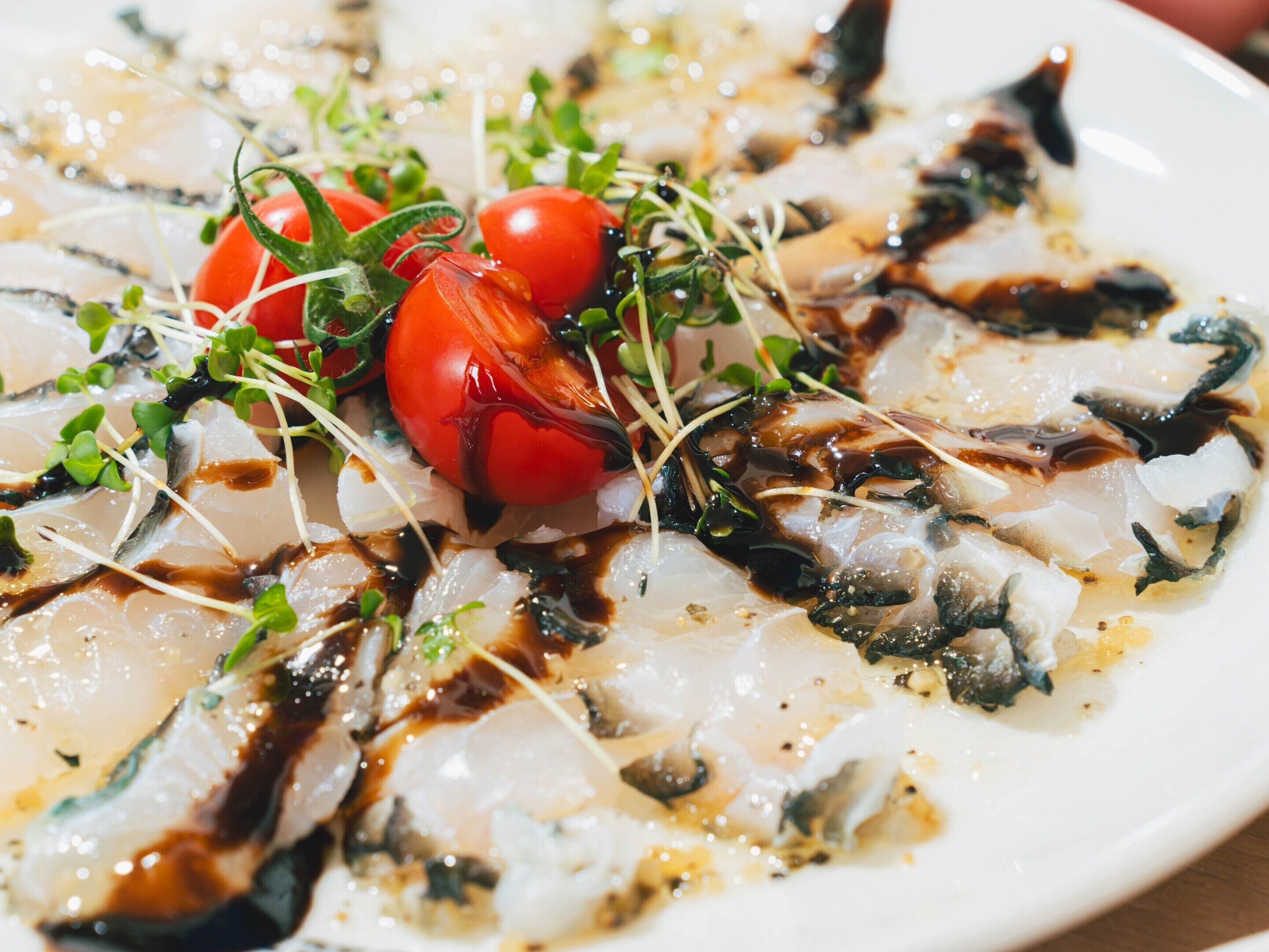 A plate of sashimi with cherry tomatoes and greens.
