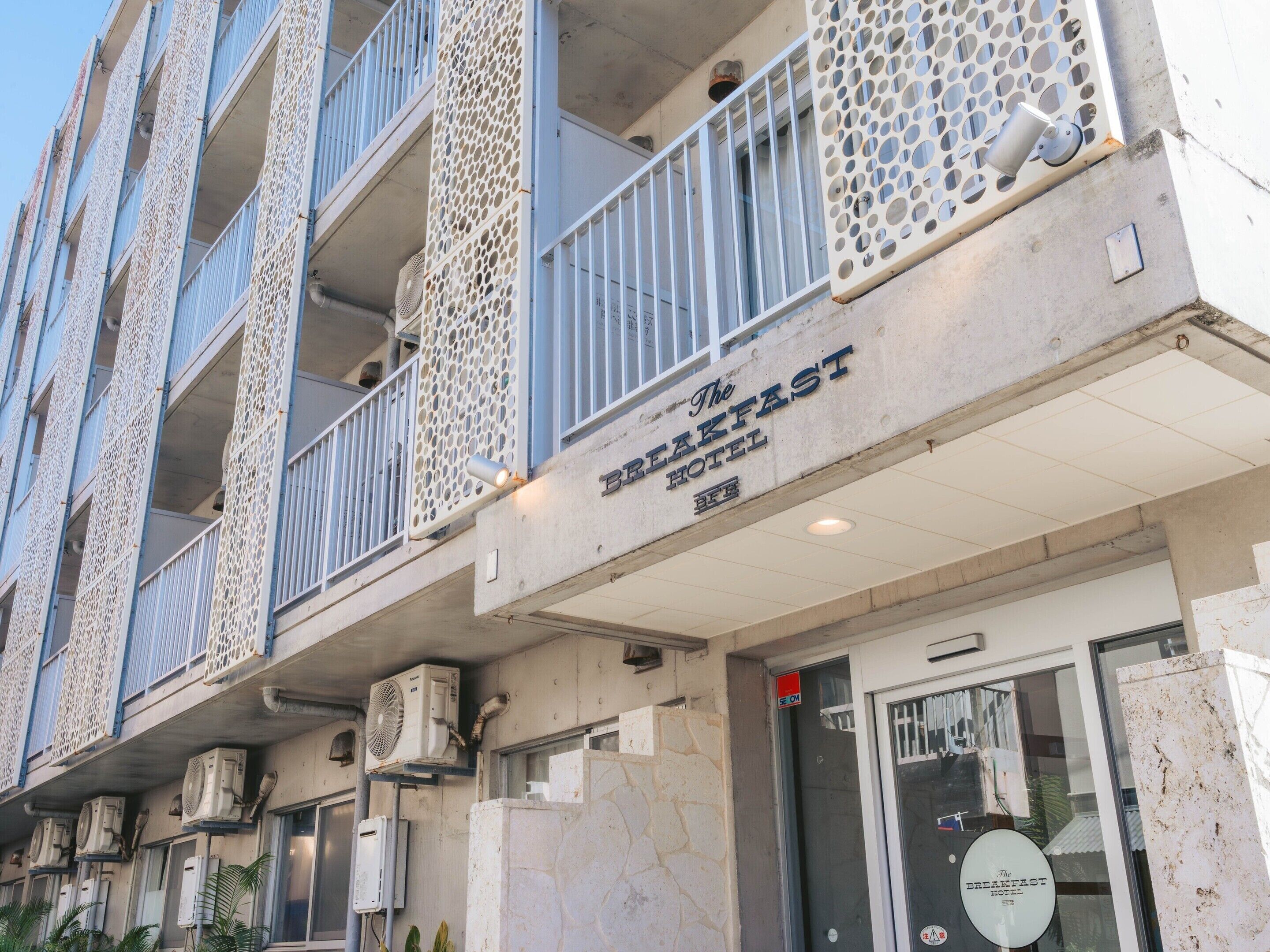 A hotel with a sign reading 'The Breakfast Hotel.' It features multiple balconies with decorative railings and air conditioning units installed on the exterior.