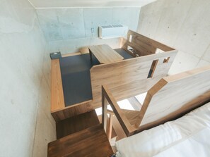 Una habitación compacta y moderna con escritorio y silla integrados, un pequeño purificador de aire blanco y una ventana que ofrece luz natural.