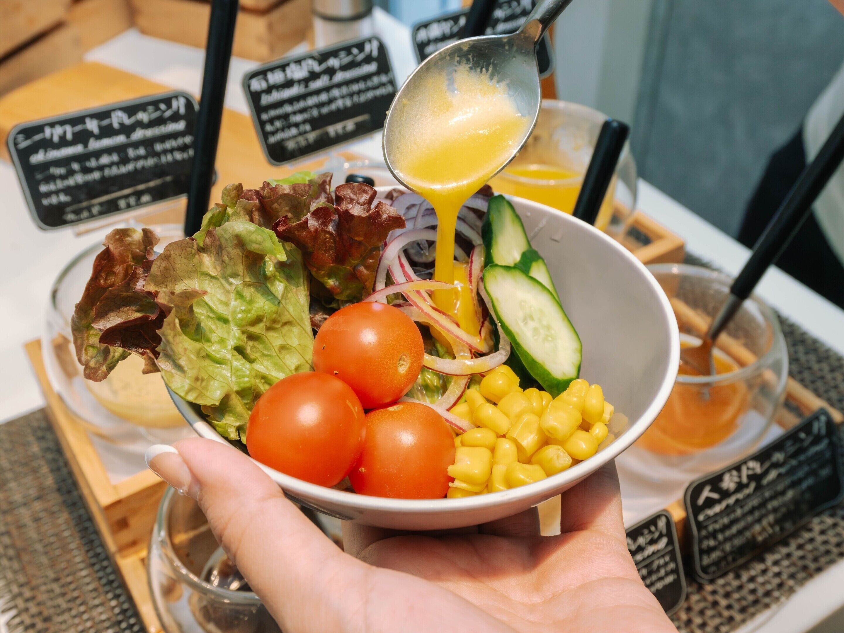 Un tazón de ensalada con diferentes verduras y una cucharada de aderezo vertiéndose.