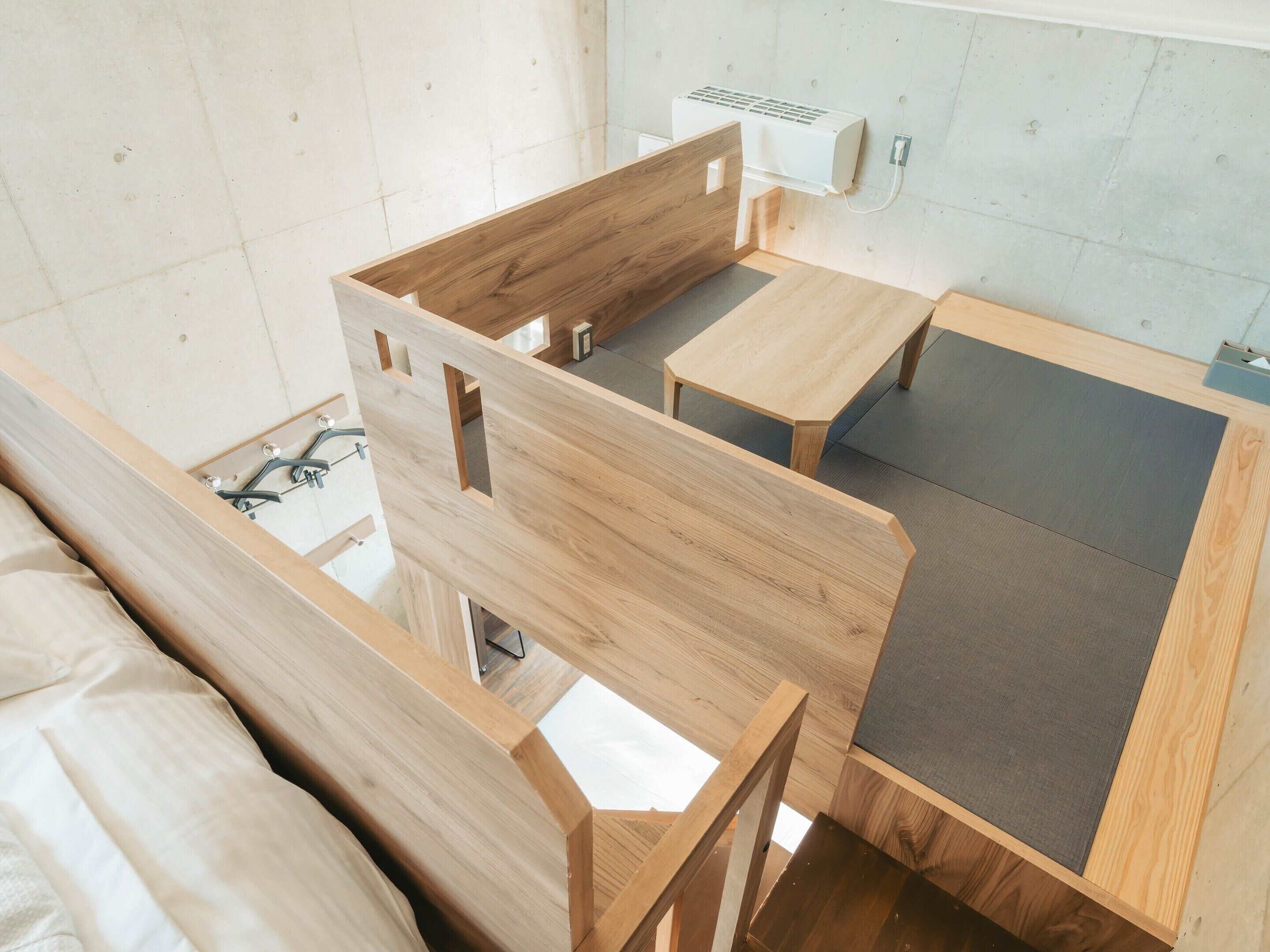 A room with a bed, a wooden bench, a small table, and a wall-mounted air conditioner.