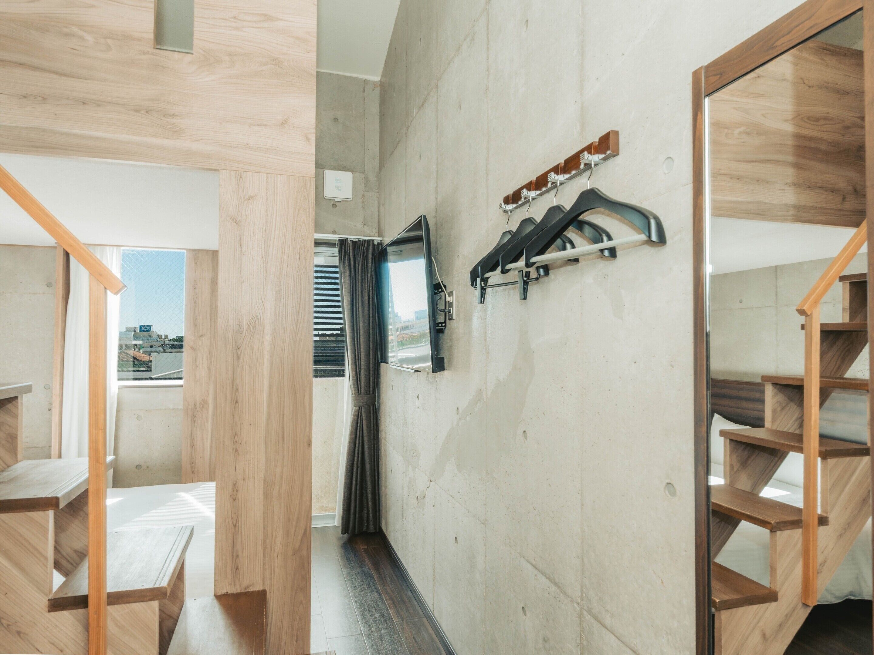 Una habitación con una escalera de madera, un ventanal con persianas y un perchero con ganchos.