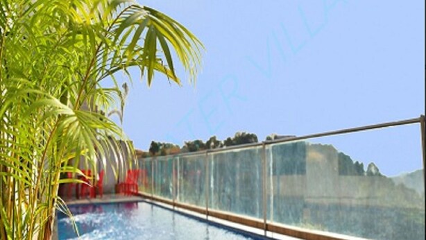 A swimming pool with a glass barrier, surrounded by palm trees and a clear sky. - SkyWater Villas And Lifestyle (Igatpuri)