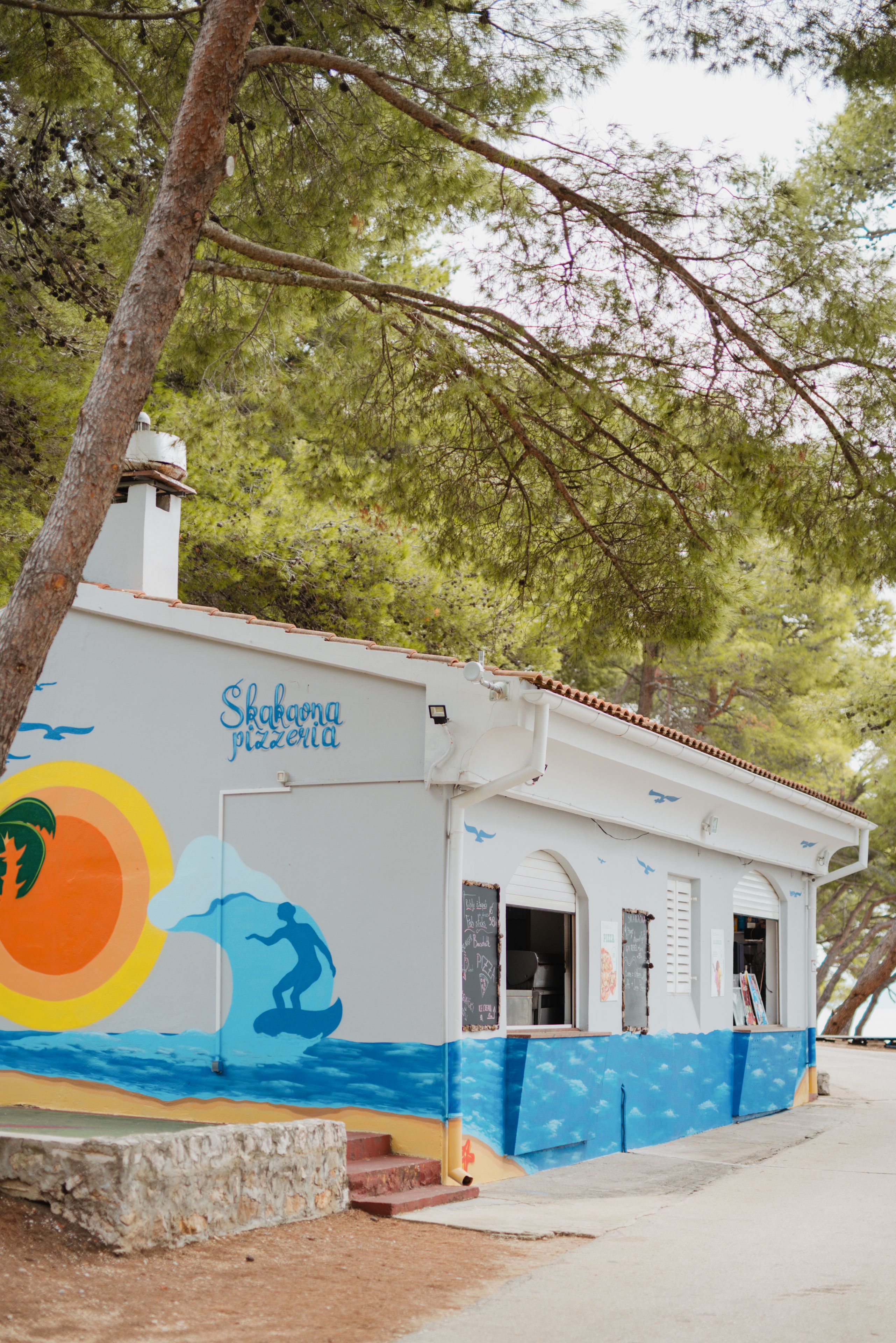 A building with a mural of a surfer and waves, labeled "Skakona pizzeria."