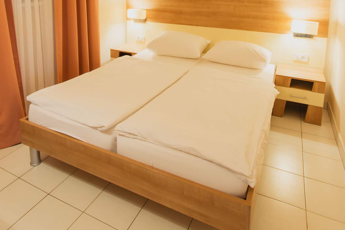 Siististi pedattu sänky hotellihuoneessa, jossa on puinen pääty, kaksi yöpöytää ja pieni sivupöytä.