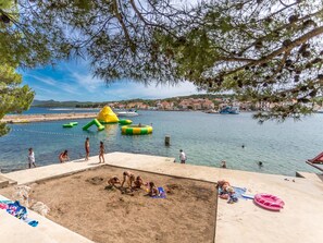 A beach with a sandy area, water, and a small hill with inflatable structures.