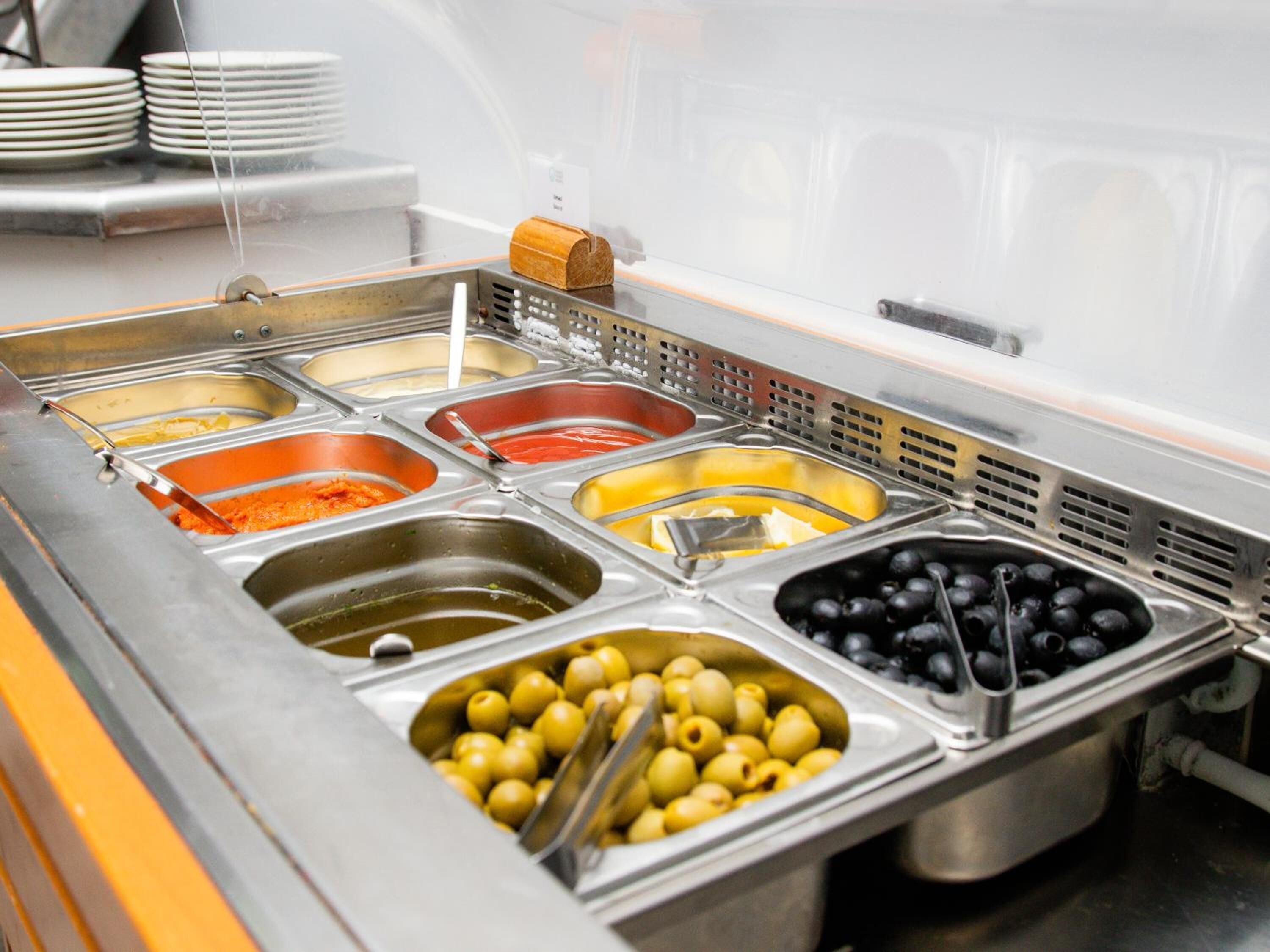 Un bufé con diversos alimentos, incluyendo aceitunas, aceitunas negras y un recipiente con salsa de naranja.