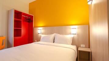 Une chambre d’hôtel avec un lit, une armoire rouge et deux lampes fixées au mur.