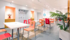 A modern dining area with white tables and orange chairs, featuring a large potted plant and a wall-mounted TV. - Hotel Première Classe Casablanca Centre Ville (Casablanca)