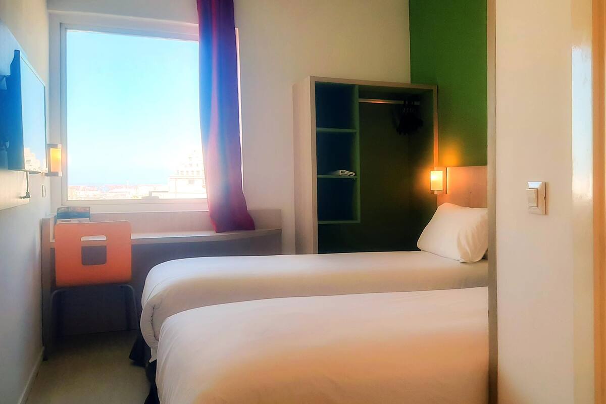 A hotel room with two beds, a window with a view, a desk, and a wardrobe.