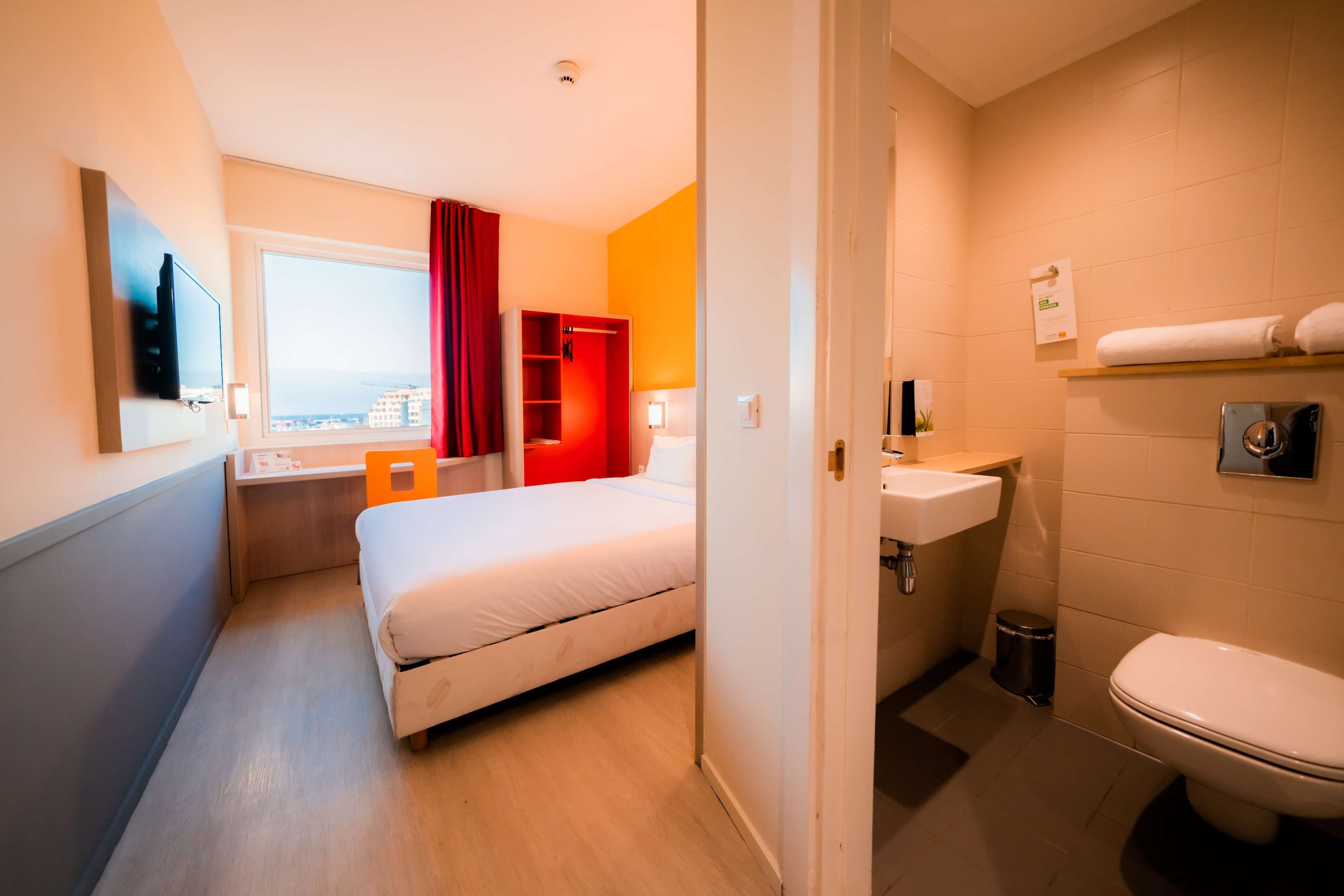 A hotel room with a bed, a desk, a window with a view, a bathroom with a sink and toilet.