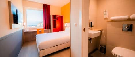 A hotel room with a bed, a desk, a window with a view, a bathroom with a sink and toilet.