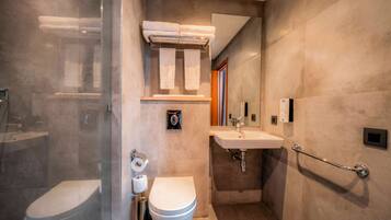 A modern bathroom with a glass shower enclosure, a toilet, a sink, and a handrail.
