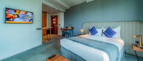 A modern hotel room with a large bed, a desk, and a television on the wall.