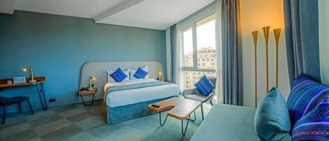 A modern hotel room with a bed, a sofa, a desk, and a nightstand.