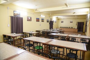Un aula con varias mesas y sillas, ventiladores de techo y carteles educativos en las paredes.