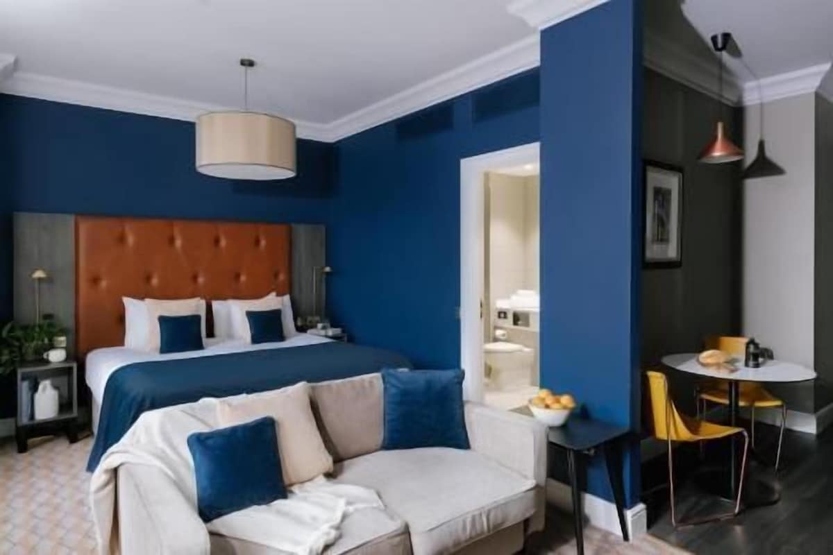 A hotel room with a bed, a sofa, a dining table, and a mirror.