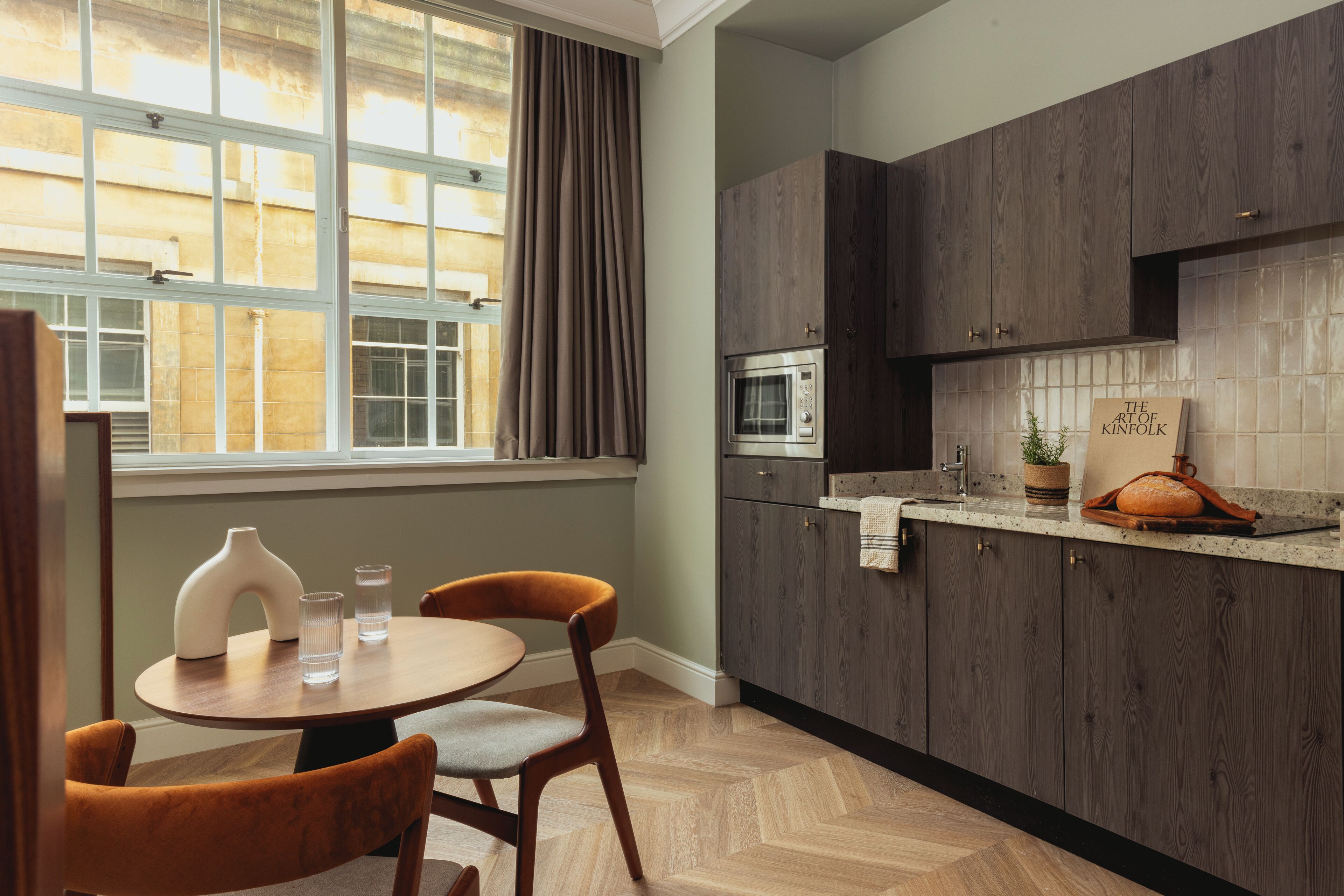 A modern kitchen with wooden cabinets, a microwave, and a dining area with a round table and two chairs.