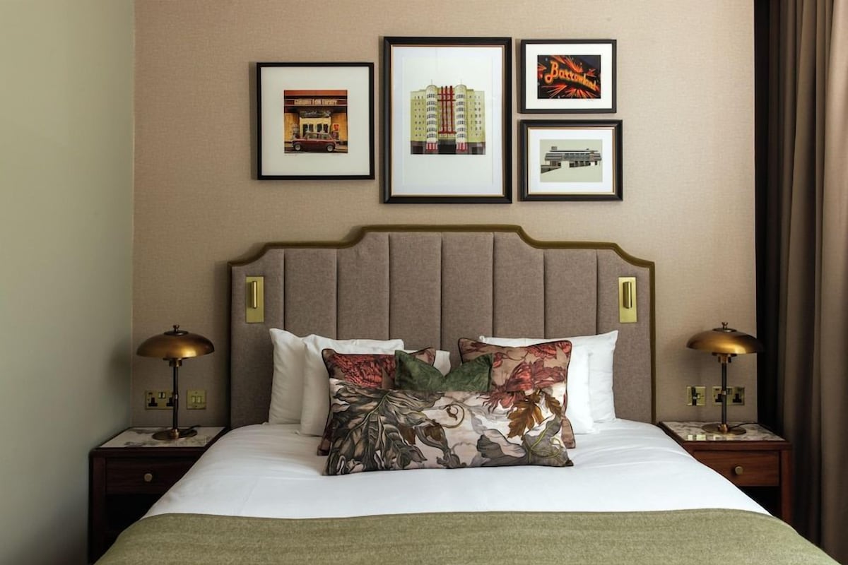 A hotel room with a bed, two bedside tables, a headboard, and three framed pictures on the wall.