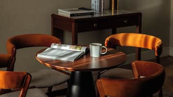 A round wooden table with a newspaper, a white mug, and books. There are two brown upholstered chairs around the table.