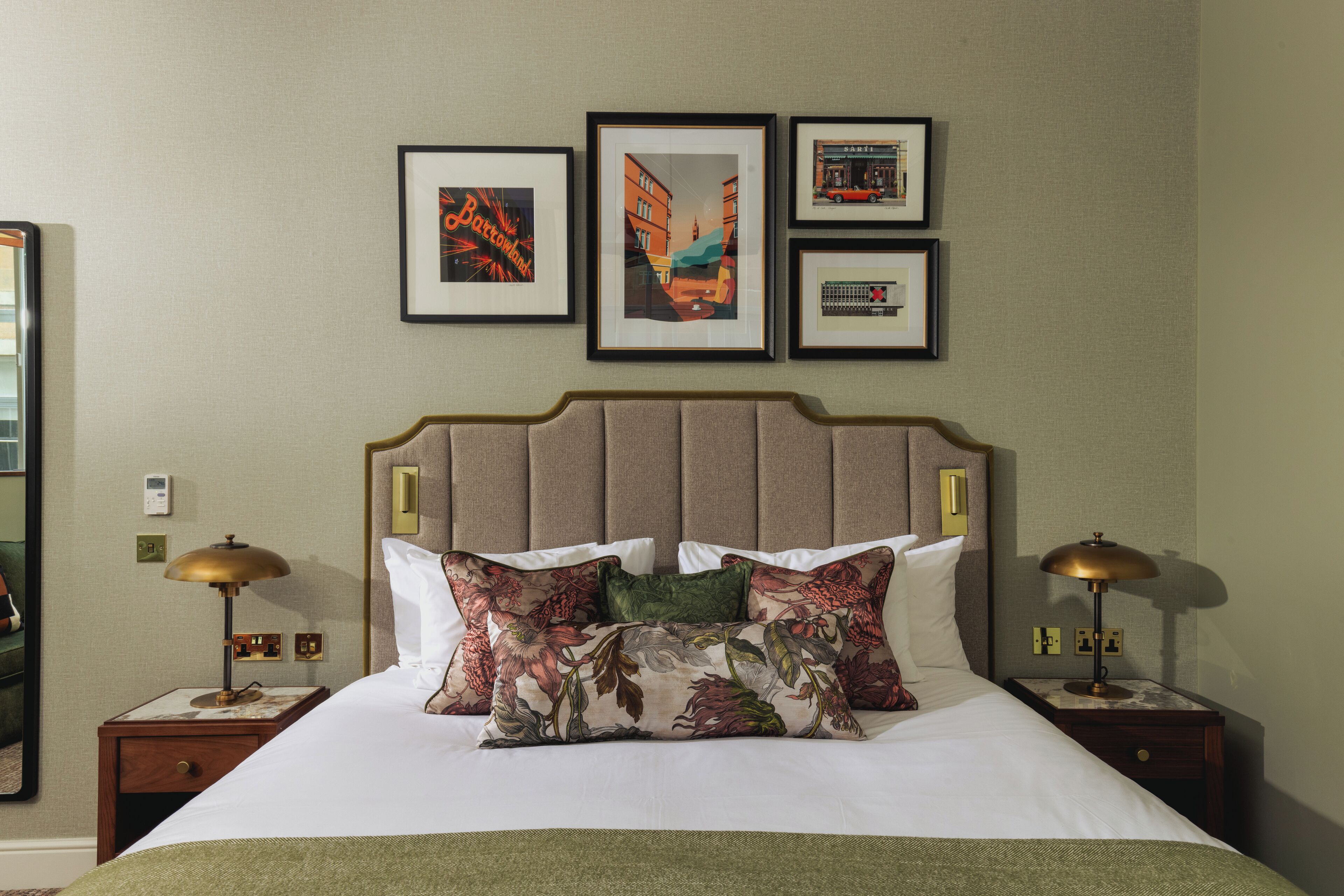 A neatly made bed with floral pillows, a headboard, and two bedside tables with lamps. There are three framed pictures on the wall above the bed.