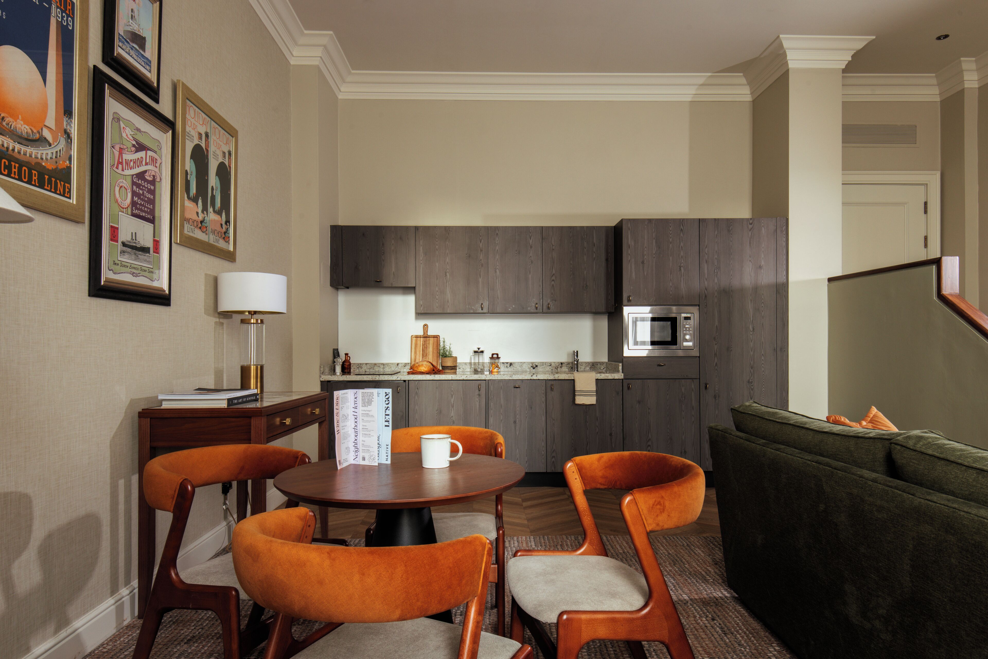 A modern kitchen with dark wood cabinets, a microwave, and a dining area with a round table and orange chairs.
