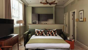 A hotel room with a bed, a desk with a television, a chair, a bedside table, a lamp, a window with curtains, a kitchenette, and a ceiling light fixture.